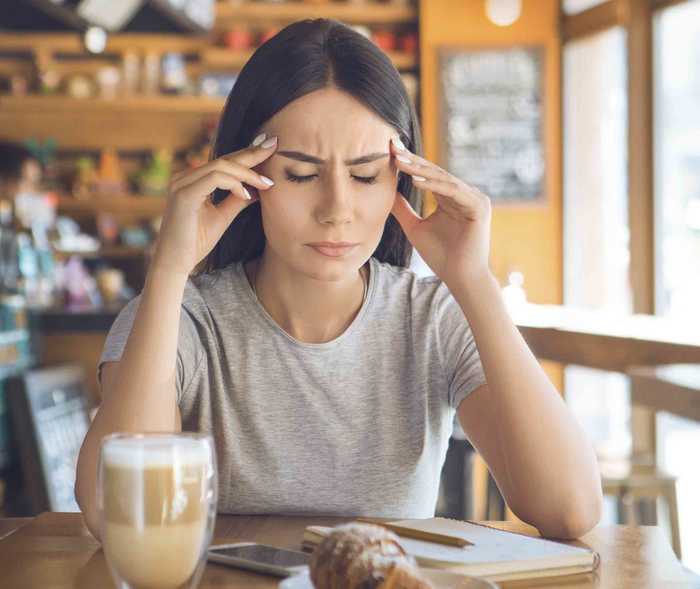 Auslöser Lebensmittel: Frau sitzt mit Migräne im Café.