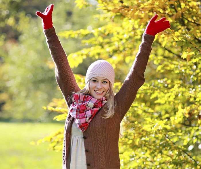 Ist Migräne heilbar? Frau steht neben Gebüsch und reckt glücklich die Arme nach oben.