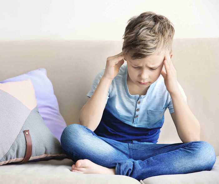 Migräne bei Kindern: Junge sitzt mit Kopfschmerzen auf Sofa