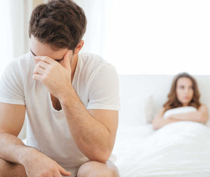 Paar im Bett: Mann leidet unter Sexualkopfschmerzen und fasst sich mit Hand an den Kopf.