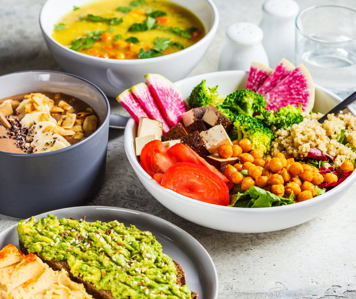 Ein Tisch mit pflanzlichen Lebensmitteln wie Tofu, Kichererbsen und Quinoa in verschiedenen Schalen.