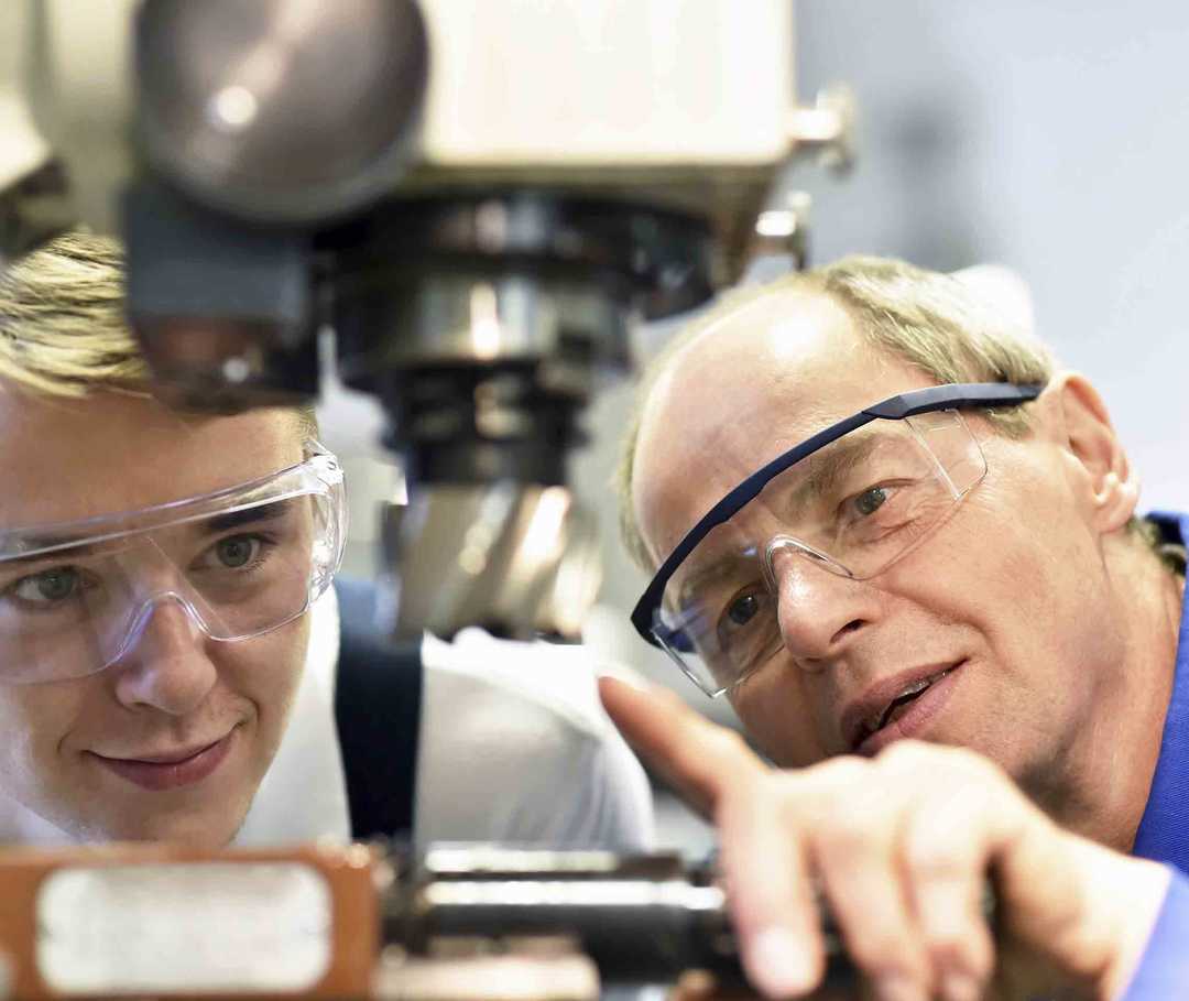 Der Ausbilder erklärt dem Lehrling, wie die Maschine funktioniert. Wegen seiner schweren Migräne ist er häufig unfähig, seinen Beruf auszuüben.  