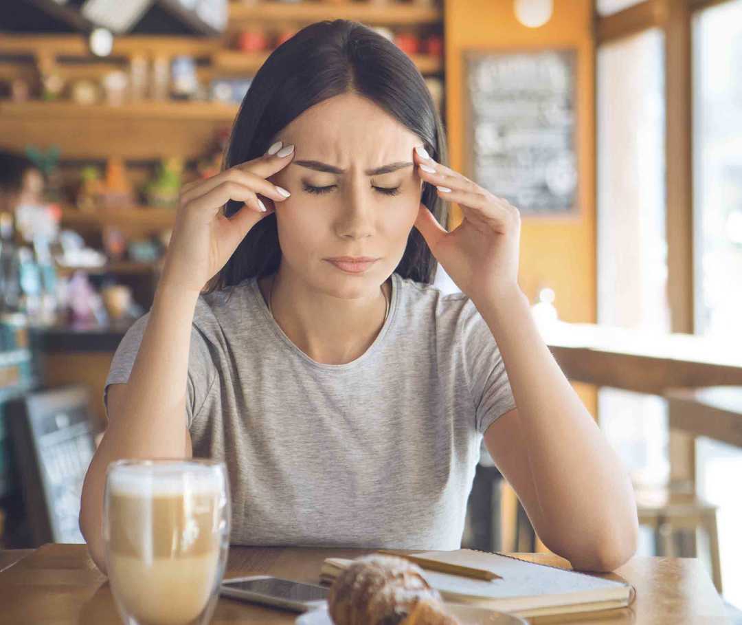 Auslöser Lebensmittel: Frau sitzt mit Migräne im Café.