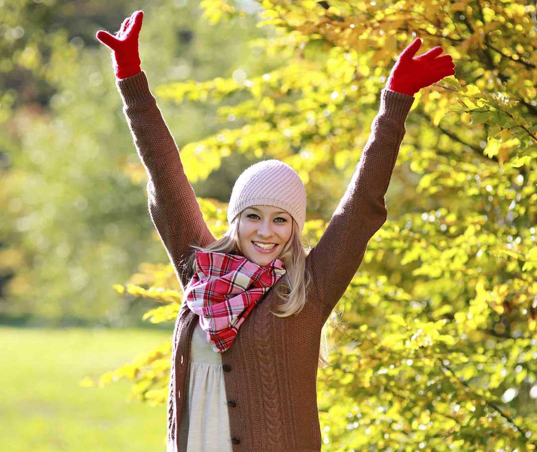 Ist Migräne heilbar? Frau steht neben Gebüsch und reckt glücklich die Arme nach oben.