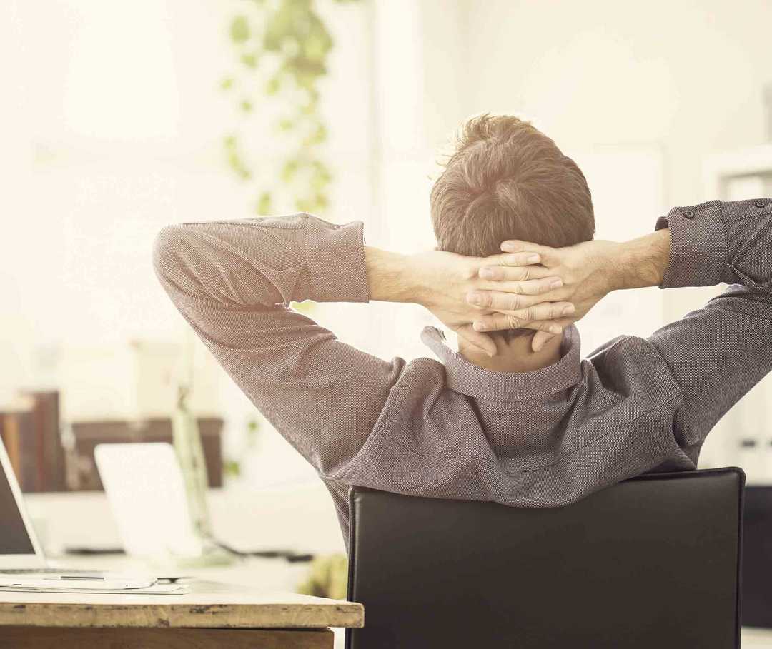 Mann sitzt auf einem Stuhl im Büro und führt eine Migräne-Übung durch.