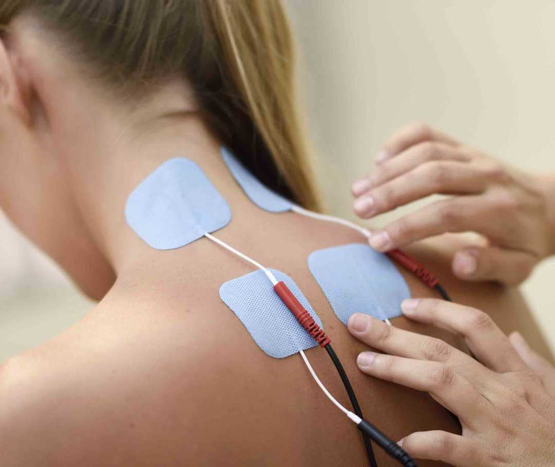 Therapeut klebt für eine Biofeedback-Therapie einer Patientin mit Migräne Elektroden auf die Haut.