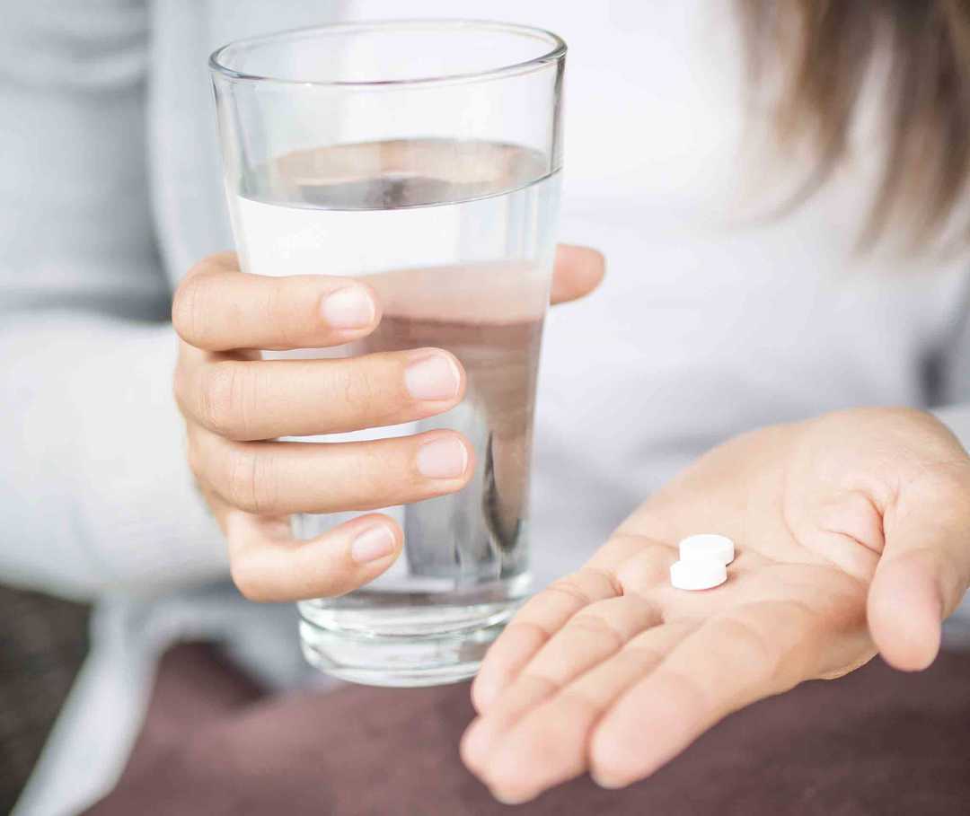 Eine Frau hält ein Glas Wasser und Schmerzmittel gegen ihre Migräne in den Händen.