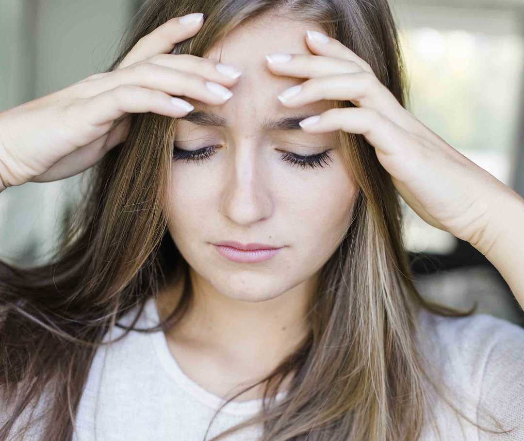 Frau hält sich den Kopf, sie leidet an episodischer Migräne.