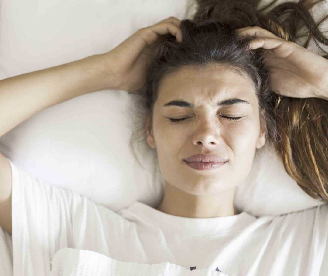 Frau mit Status migränosus liegt wegen ihrer starken Kopfschmerzen im Bett.