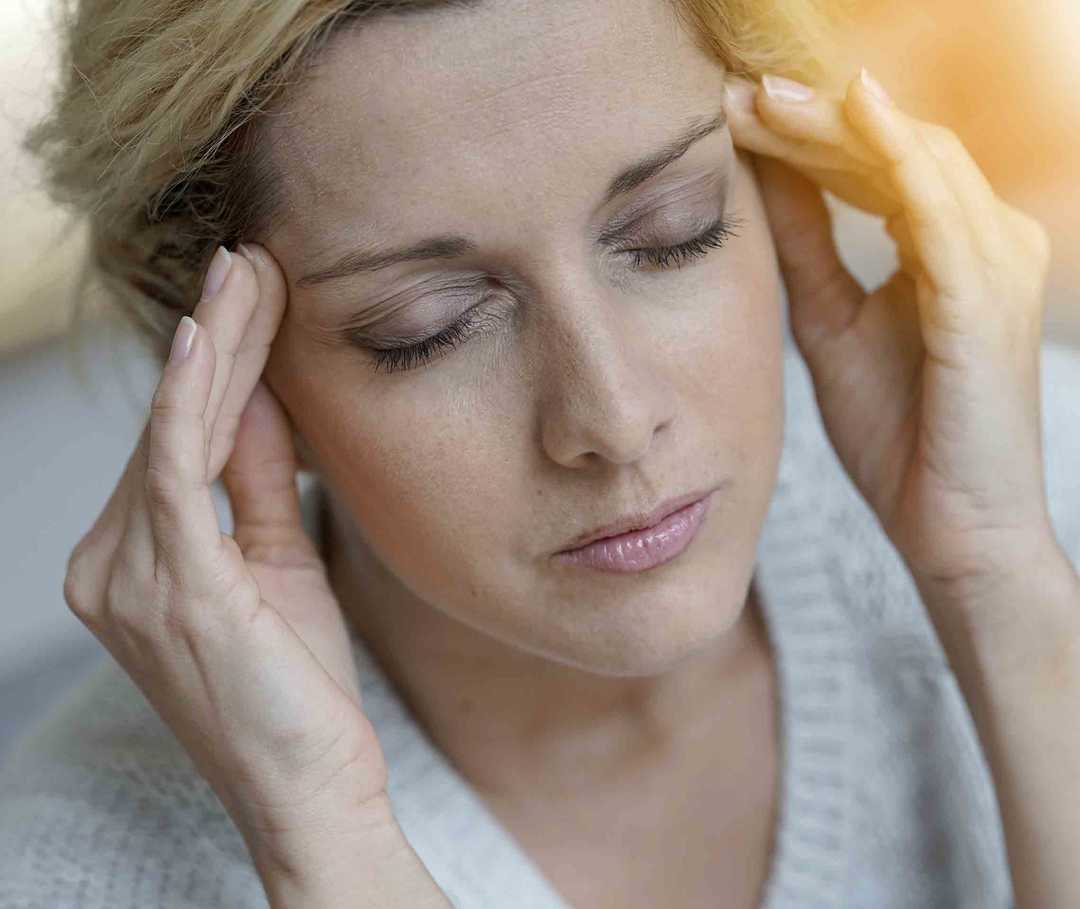 Frau, die an Migräne mit Aura leidet, hält sich vor Schmerzen den Kopf.