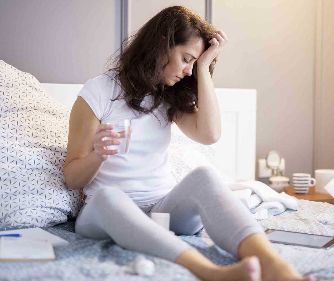 Frau sitzt auf dem Bett mit Kopfschmerzen und Schwindelgefühlen – Anzeichen der vestibulären Migräne.