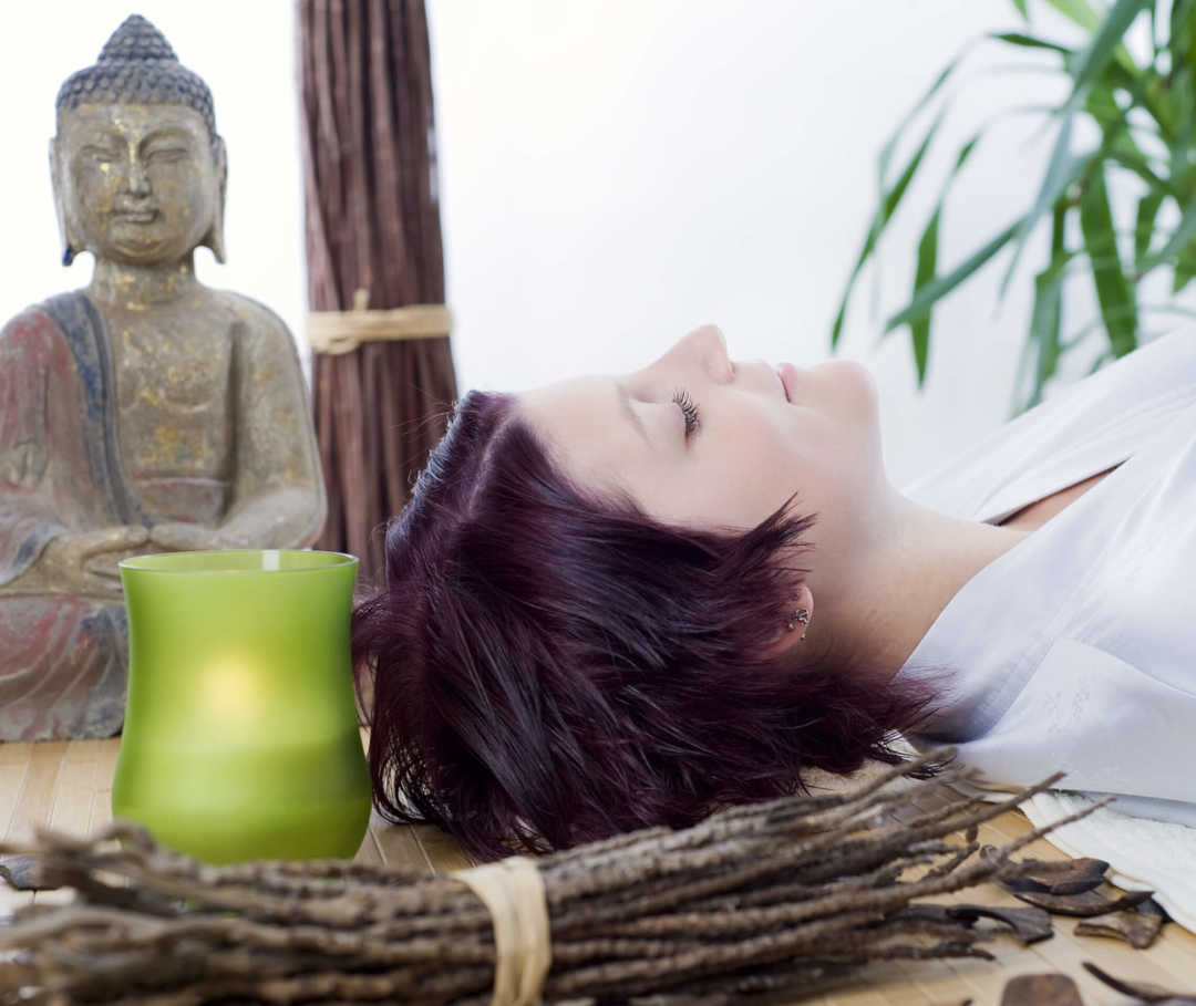 Autogenes Training gegen Migräne: Frau liegt auf dem Rücken mit Kerze neben sich.