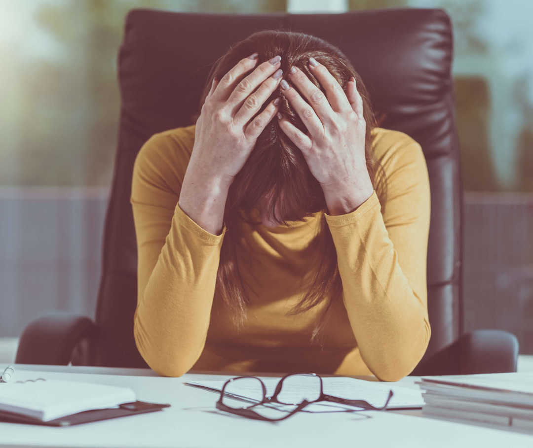 Frau sitzt am Schreibtisch und leidet an Migräne aufgrund einer Reizüberflutung durch Licht.