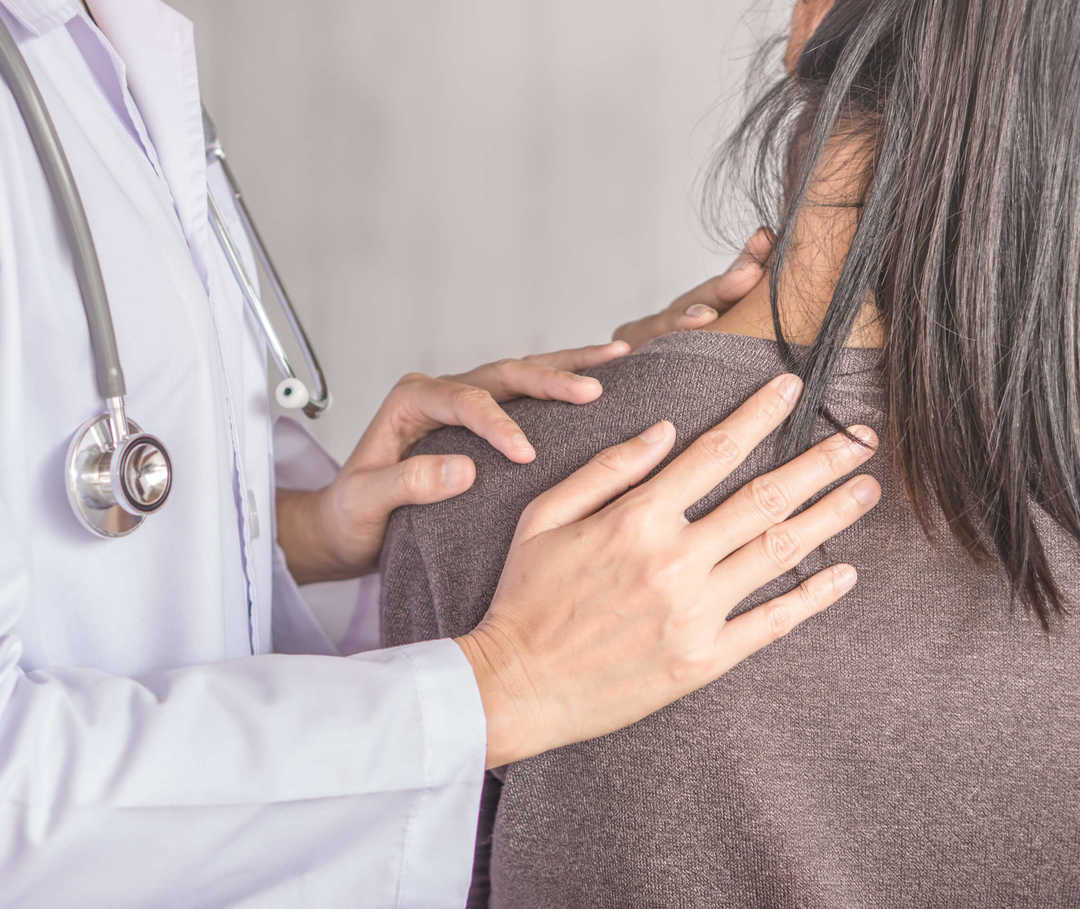 Arzt untersucht den Nacken einer Frau, die unter Spannungskopfschmerzen leidet.