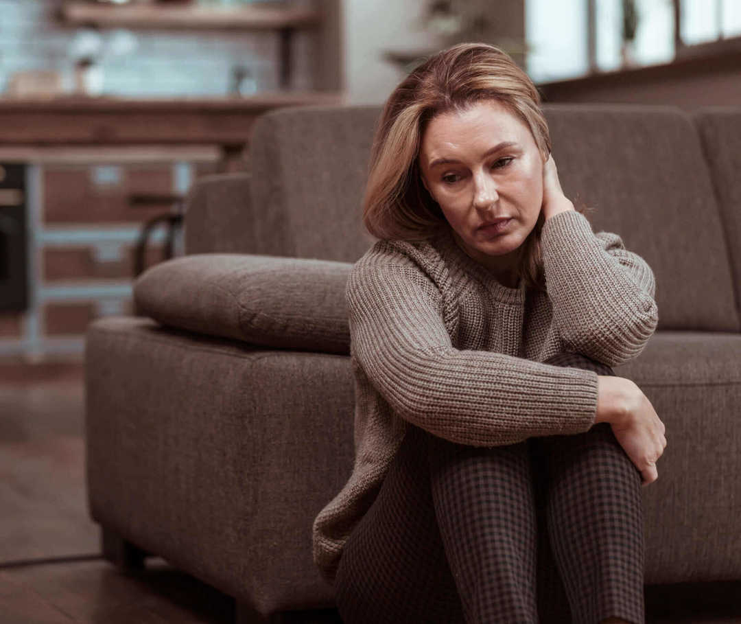 Frau mit Migräne und Depressionen sitzt vor ihrem Sofa.