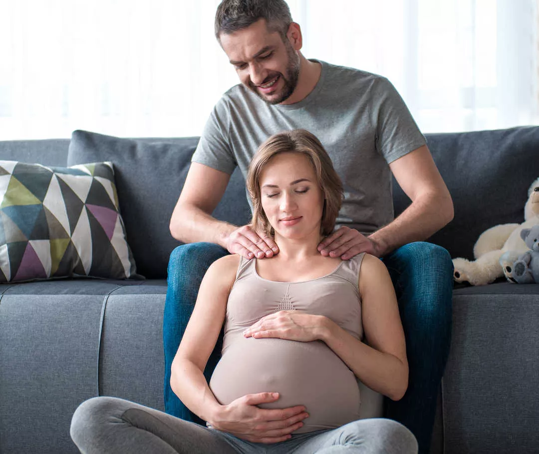 Nach dem Vorbereitungskurs massiert ein Mann seiner Frau kurz vor der Geburt die Schultern, um Migräne zu vermeiden.