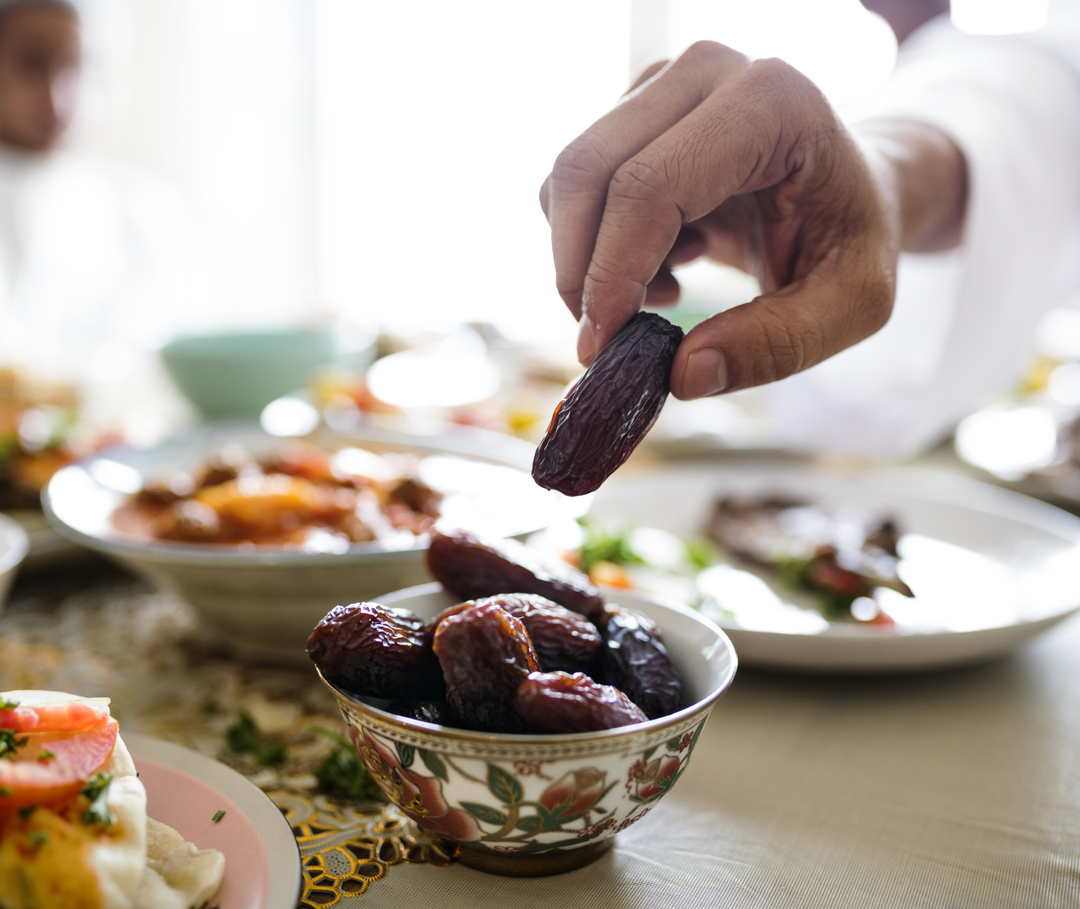 Eine Hand nimmt eine Dattel von einem reich gedeckten Tisch.