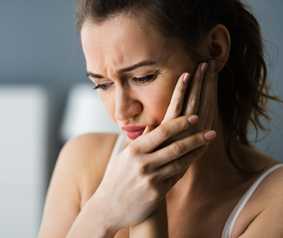 Eine Frau mit schmerzverzerrtem Gesicht hält sich die linke Wange.