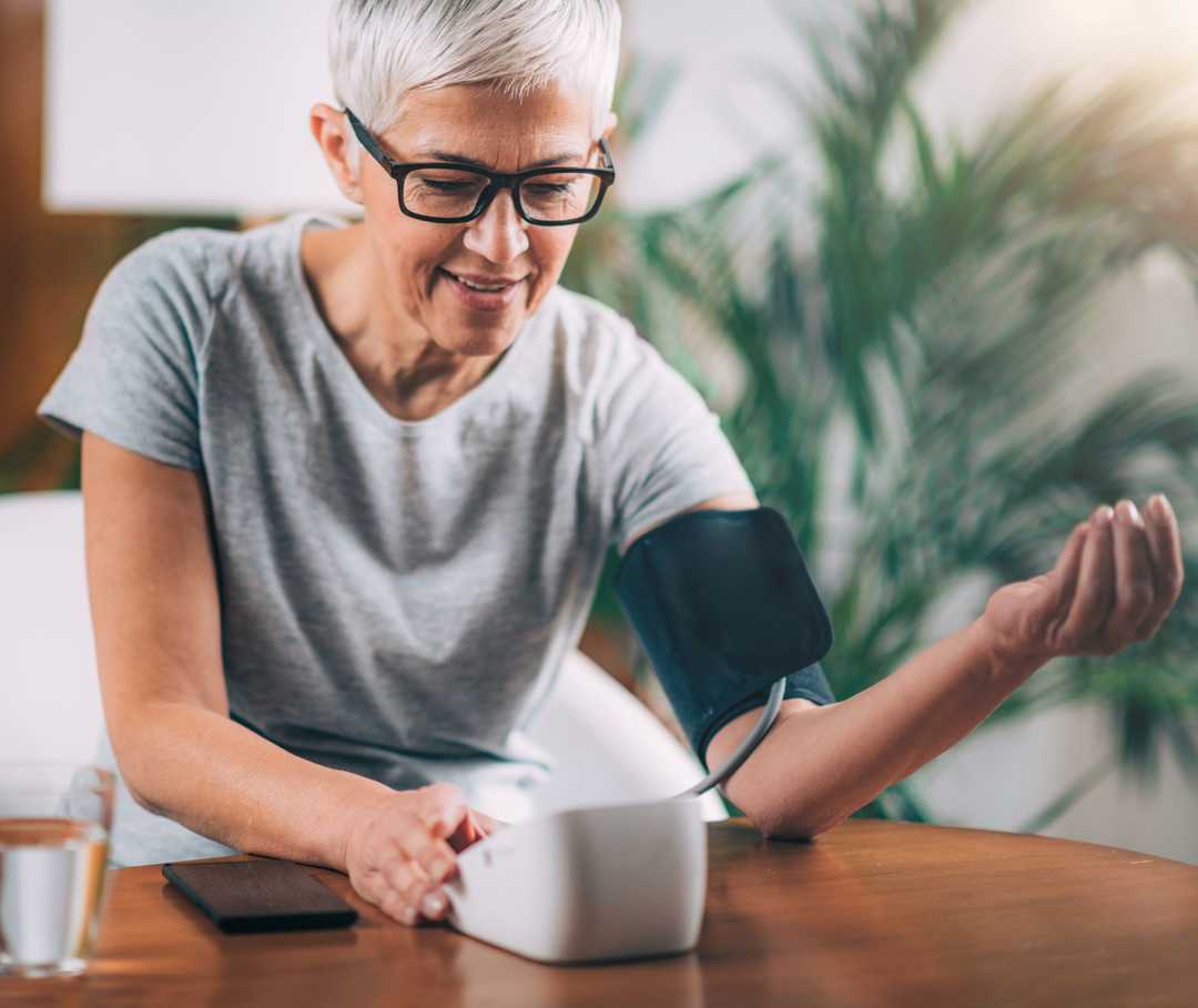 Eine Frau misst mit einem Blutdruckgerät ihren Blutdruck über eine Oberarmmanschette.